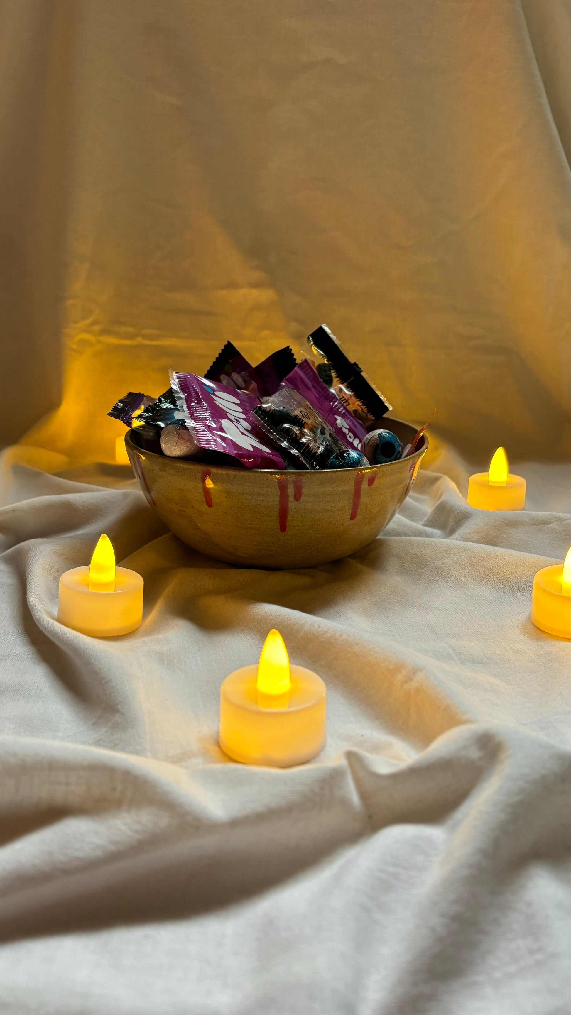 Bowl de cerámica artesanal Hecho por Su, pintada a mano, decorado color hueso y rojo, relleno de caramelos, rodeado de luces de vela tipo LED. 
