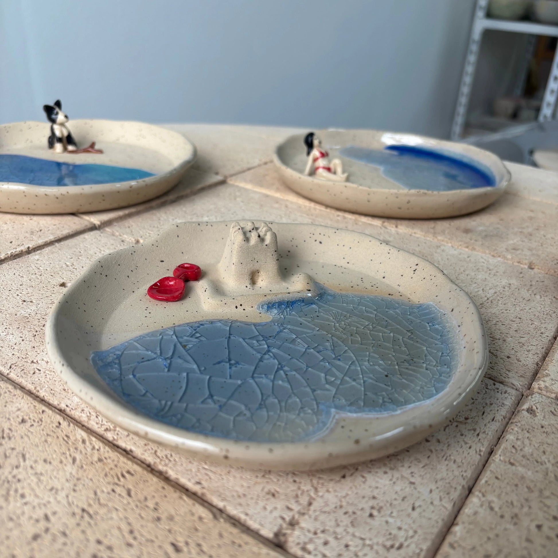Platos de cerámica artesanal de Hecho por Su con castillo de arena, playa azul pintada a mano y detalles personalizados.