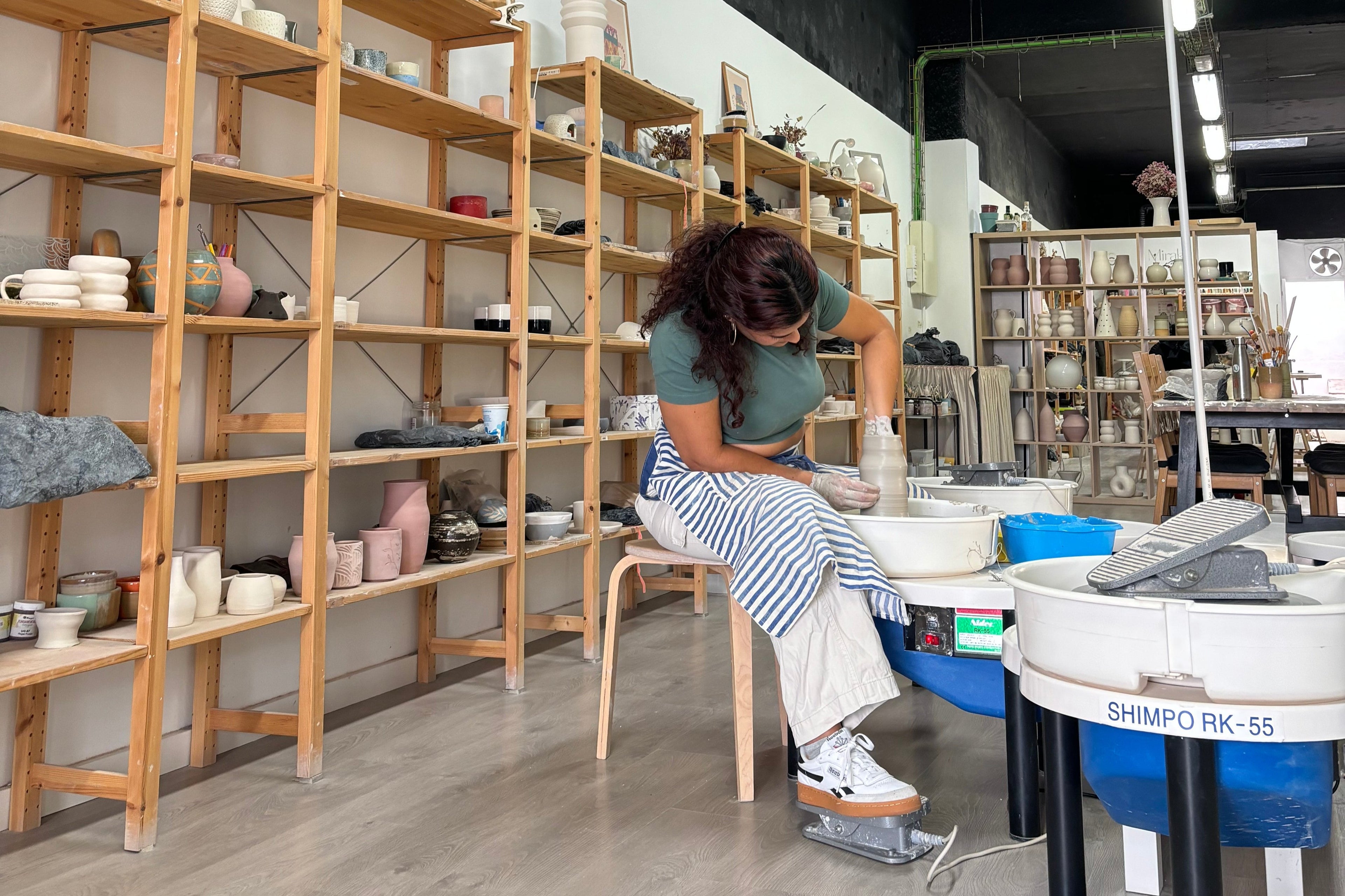 Vista del taller de Hecho por Su con las estanterías repletas de nuevas cerámicas y Su trabajando en el torneado de un jarrón.
